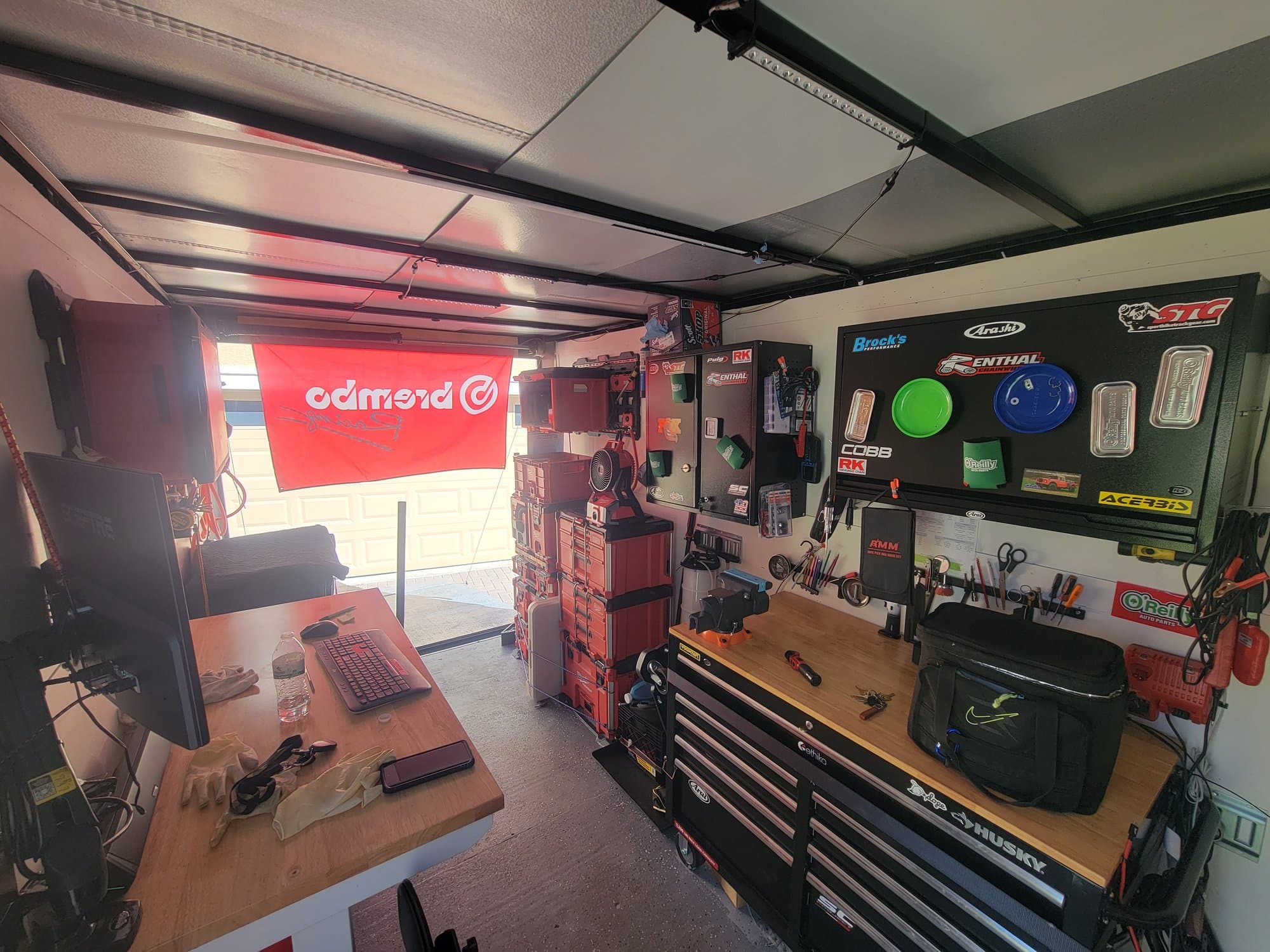 Inside the trailer: a wooden workbench with a monitor and keyboard down one side, a black rolling tool chest and a pegboard of hand tools down the other, and the stacked red tool cases and Brembo banner at the open door
