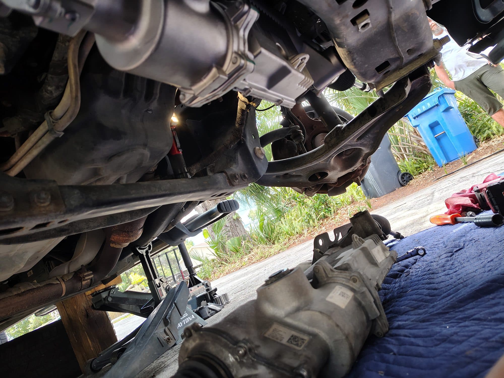Looking up under a truck raised on jack stands with the transmission removed, the unit sitting on a moving blanket on the driveway beside it